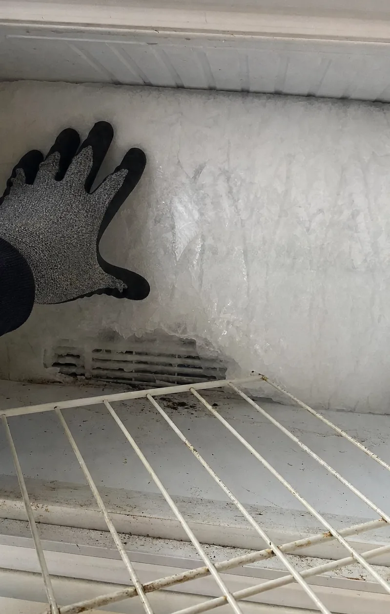 A freezer compartment iced over after an extended period without power, the frost broken away in one place to show the liner underneath.
