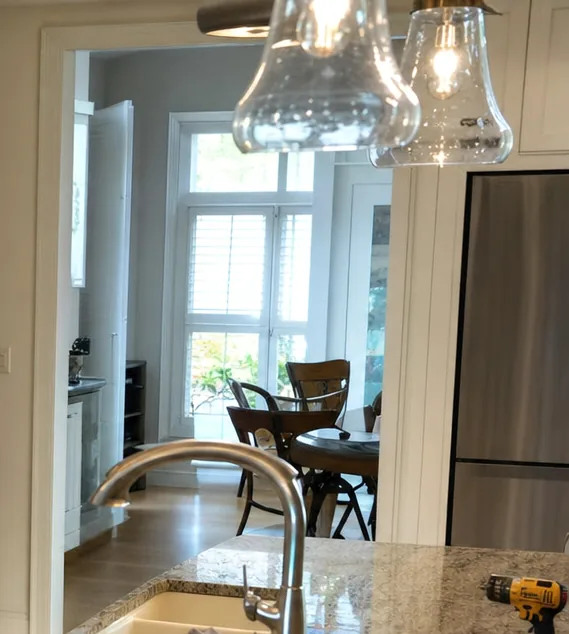 The upper part of a kitchen doorway with glass pendant lights, shuttered windows and a dining table beyond, the top corner of a stainless refrigerator at the right.